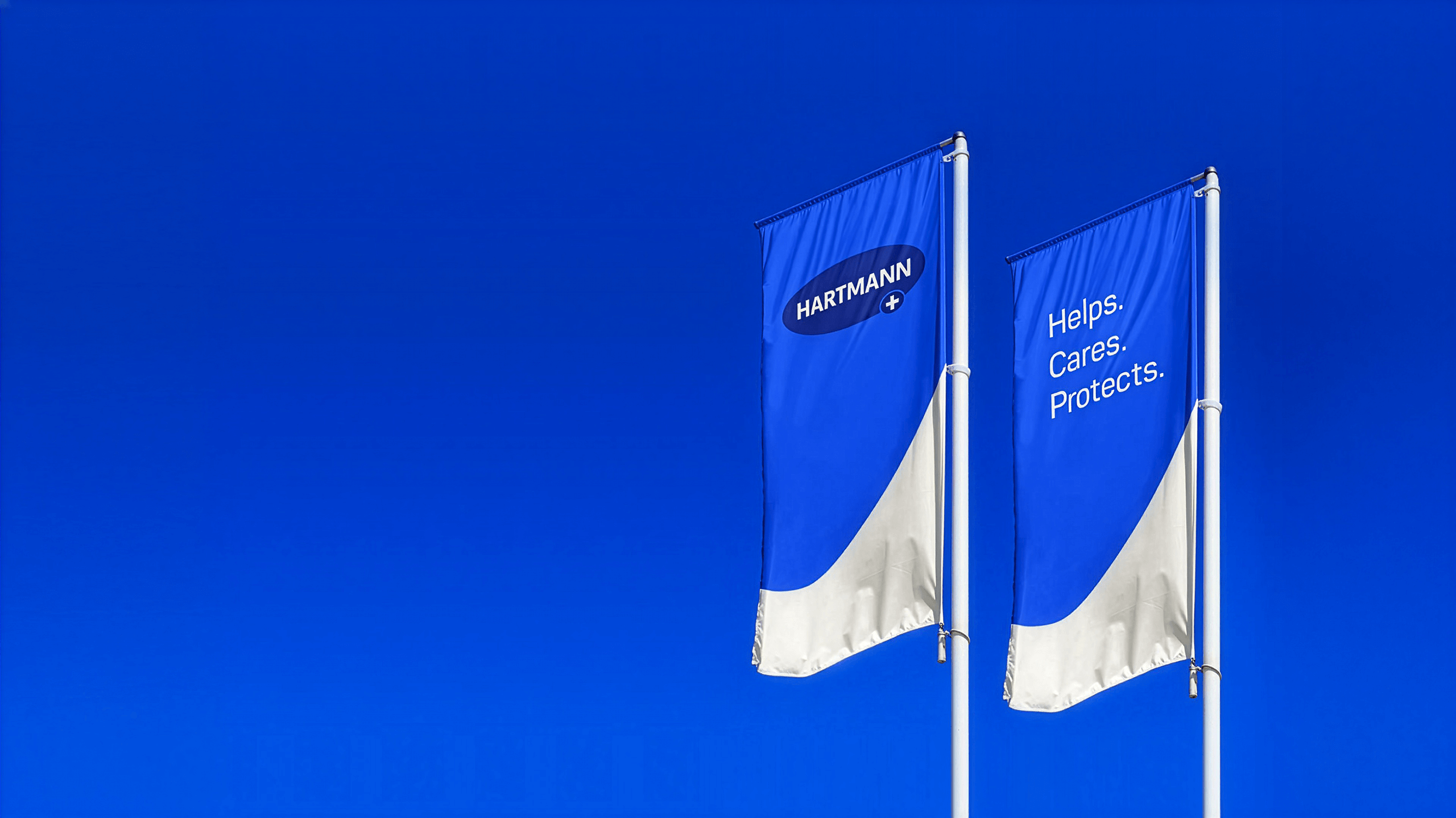 Two blue flags with HARTMANN lettering and the HARTMANN slogan "Helps. Cares. Protects."