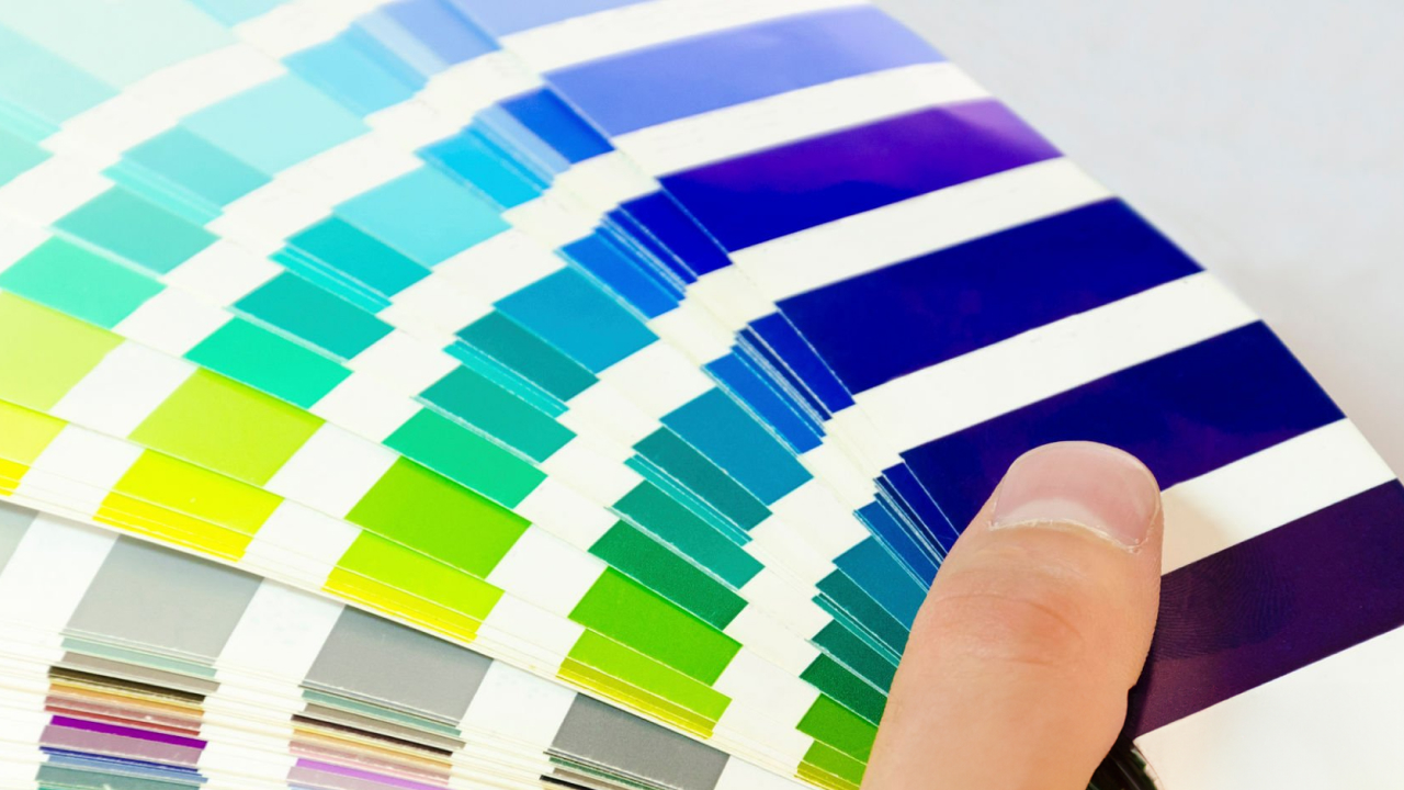 Close-up of a hand flipping through a color swatch book with shades of blue, green, and gray.