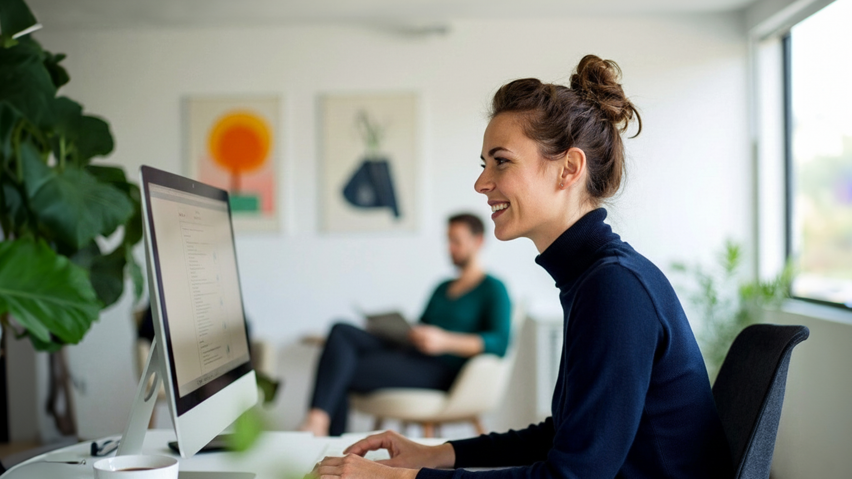 A woman smiles while working at a computer in a bright, modern office.